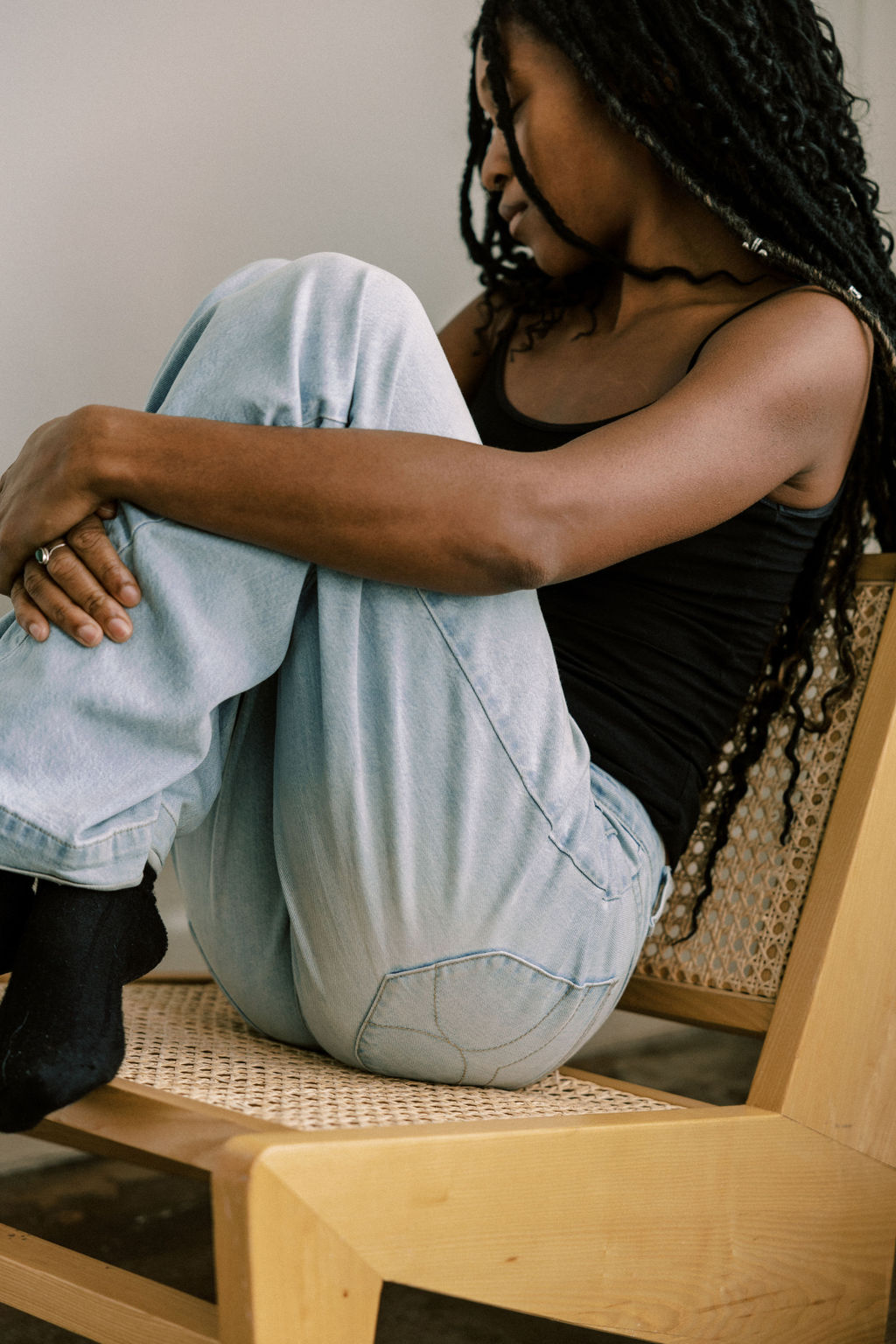 A young woman sitting on a wooden chair hugging her knees in a relaxed pose, representing introspection and therapy process